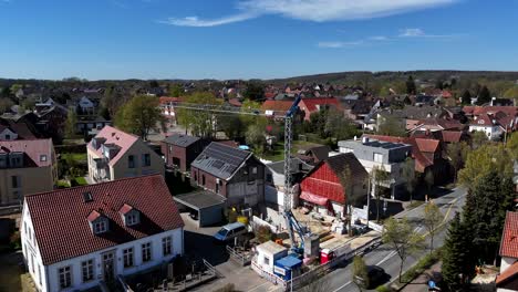 crane on construction site with crane in small german city during sunny day in spring season. aerial orbit shot. driving cars on street. modern houses with solar panels on roof.