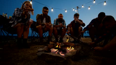 grupo de amigos viajeros fritando salchichas en el campamento
