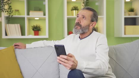 Sympathetic-old-man-sitting-on-sofa-at-home-and-texting-on-smartphone.