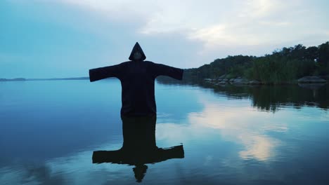 Evil witch in black cloak with hood in the river. Halloween costume.