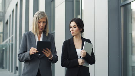 mature businesswoman reading a business project on a tablet and talking with her colleague while walking in the street