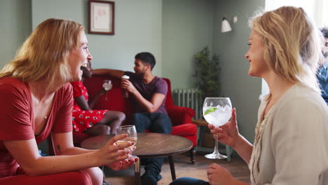 Two-young-adult-white-women-sit-laughing-together,-talking-and-drinking-wine-in-the-lounge-room-at-a-pub,-close-up