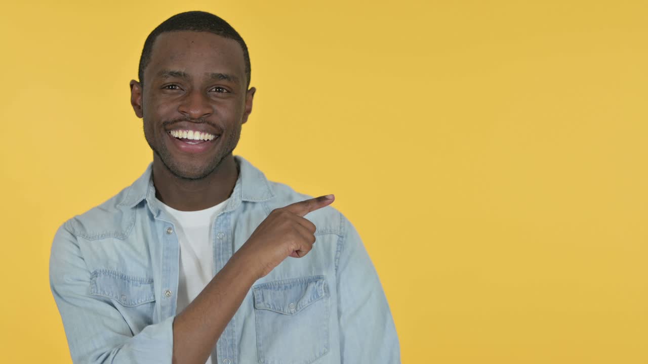 Young African Man Pointing at Product, Yellow Background