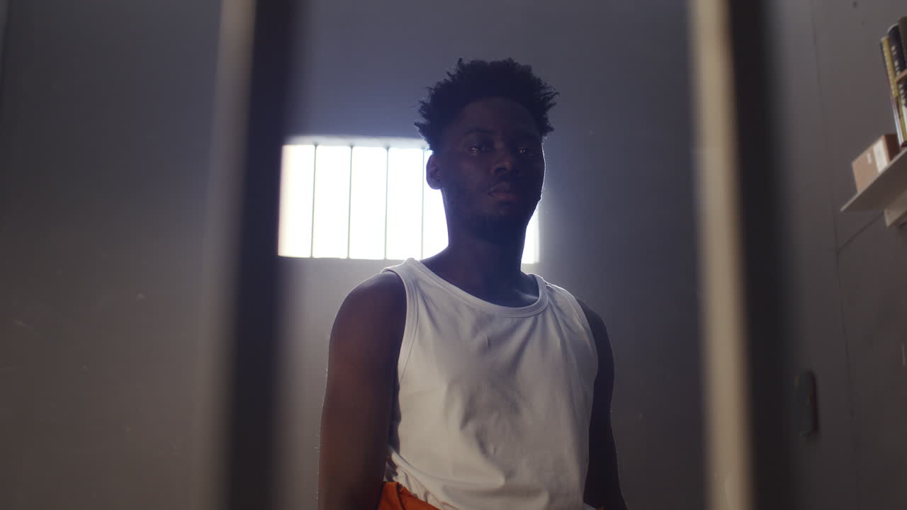 Portrait of Young Black Prisoner Standing in Cell behind Bars