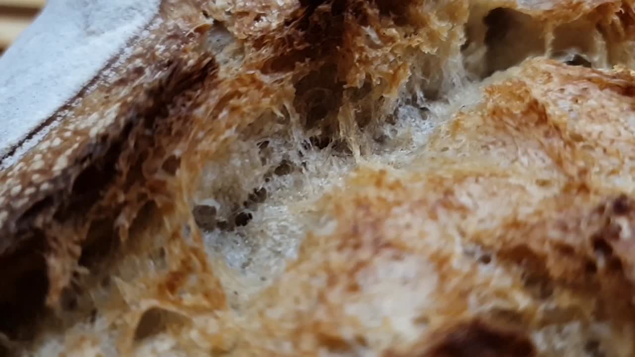 Closeup of delicious and crunchy bread crust. Review of a fresh loaf of bread. Beautifully golden baked bread made with sourdough on wooden table. Homemade sourdough crusty bread.