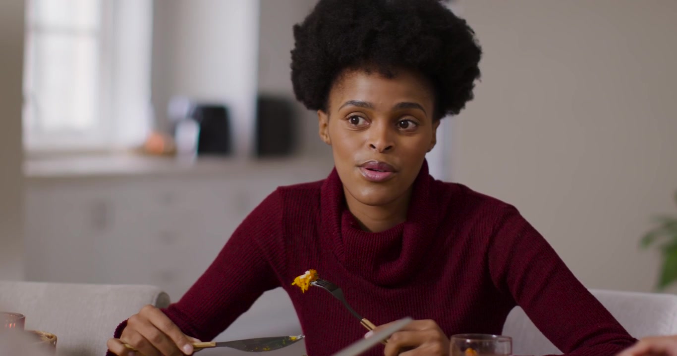 African American woman listening and replying to offscreen voice while using fork at kitchen table