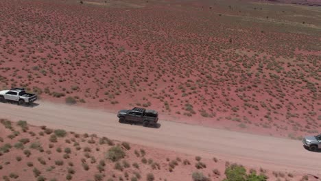 tracking aerial: trucks convoy across expanse of red scrub desert road