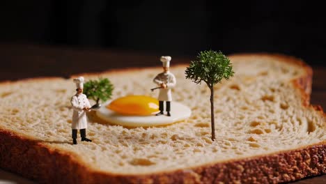 two miniature chefs are standing on a slice of whole wheat toast, collaborating on a perfectly fried egg, with miniature trees completing the whimsical scene