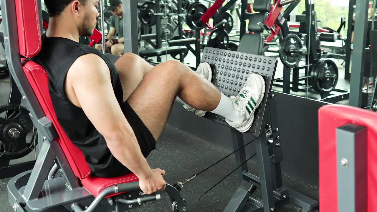A man performs leg presses in a gym, showcasing strength training. Bright lighting highlights the modern fitness environment