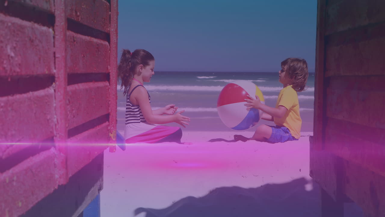 핑크와 파란색 빛 트레일 백인 형제와 여동생이 해변에서 해변 공으로 놀고 있습니다.