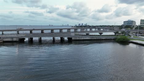 aerial approaching shot of bridges with driving cars in tampa, florida at dusk. bayshore with skyline in background. wide shot. cloudy day in usa.