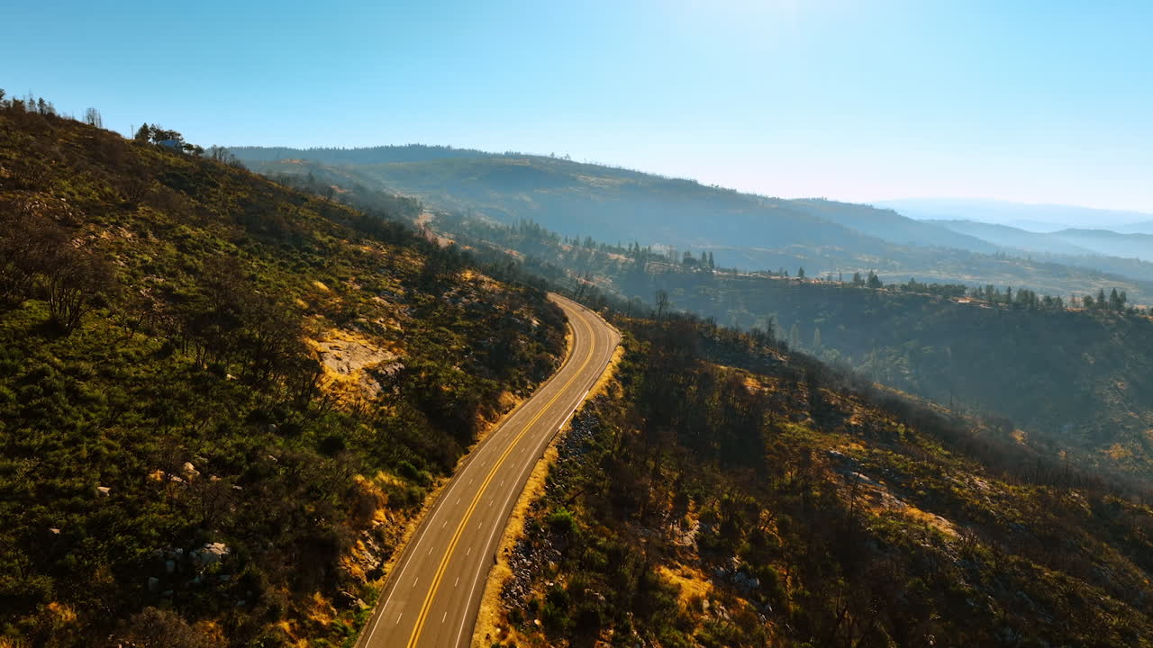 Flying above the sunlit highway in the mountains. Sunny day footage in Sierra National Forest, California, USA.