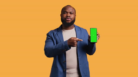 man presents phone with green screen display, isolated over studio background