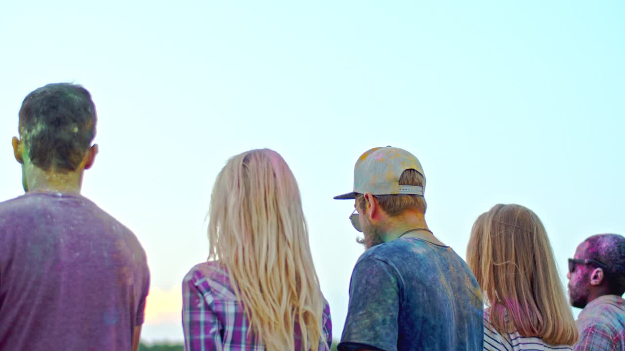 홀리 페스트 동안 야외에 서서 다채로운 페인트를 하늘에 던지는 젊은 다민족 친구들의 뒷모습