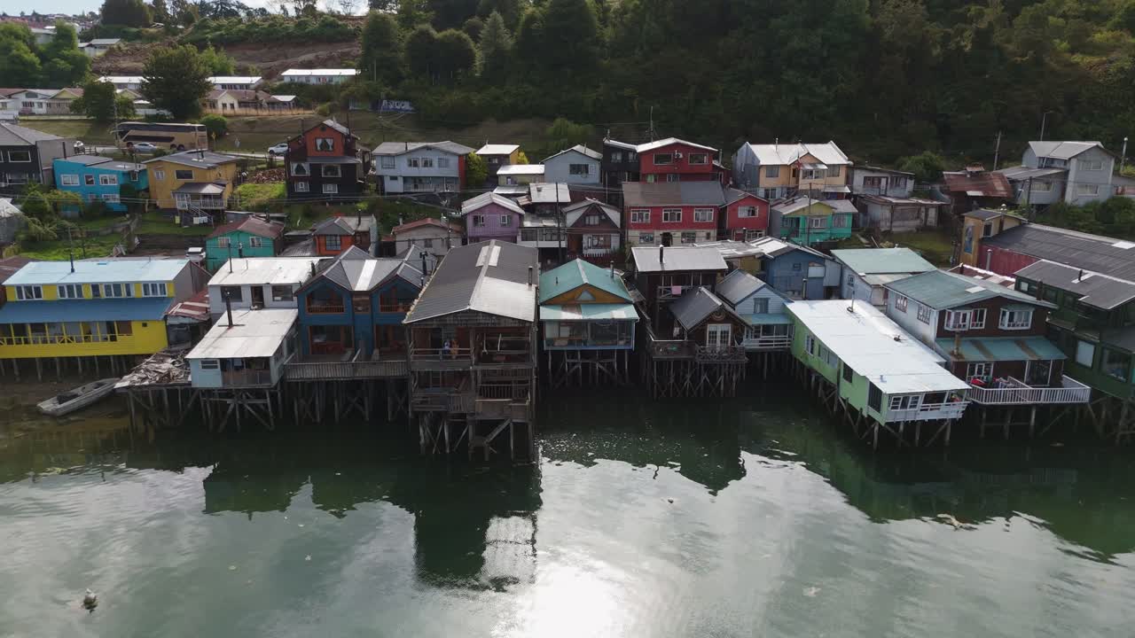 Aerial view of Vibrant stilt houses reflected on waterfront in Castro, Chiloé Island, surrounded by nature. dolly left