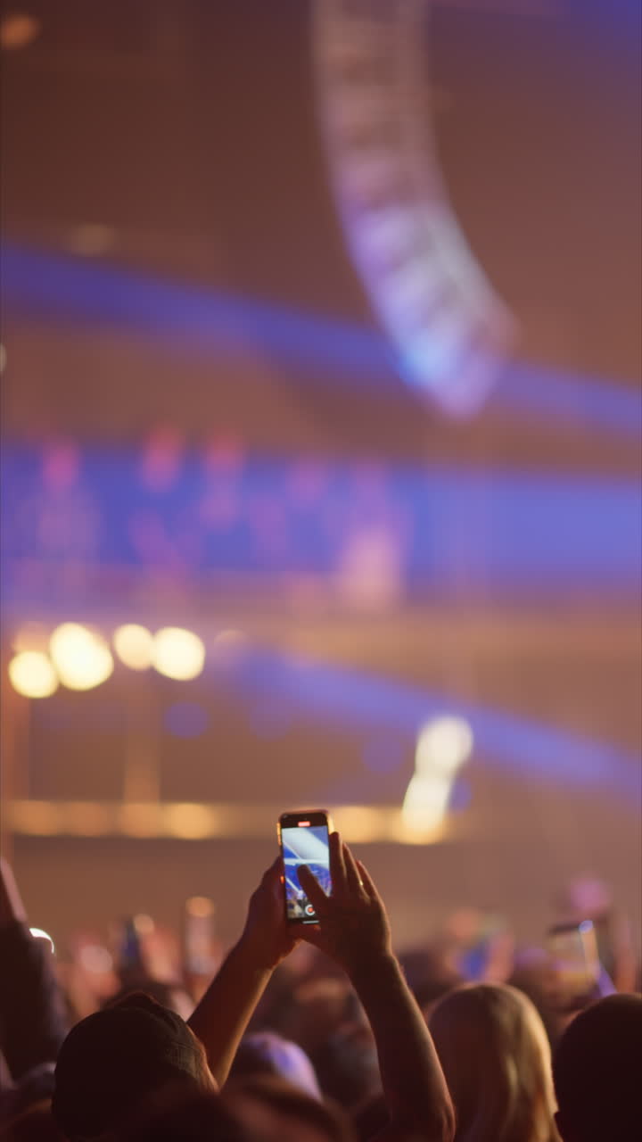 Mani che tengono uno smartphone mentre riprendono un concerto dal vivo con luci di scena dinamiche