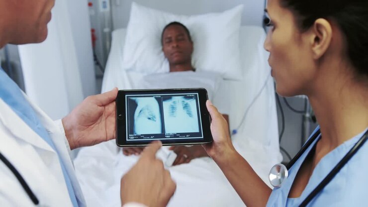 Primo piano di medici multietnici che discutono un referto radiografico su un tablet digitale in reparto, in ospedale.