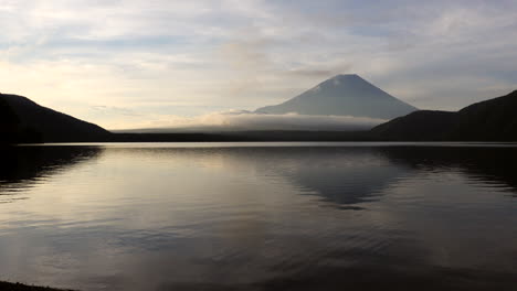 in the soft first light, the camera pans, revealing lake motosu's mirror-like surface, mirroring the serene grandeur of mount fuji