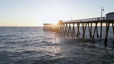 Vuelo-Aéreo-Que-Muestra-La-Silueta-Del-Embarcadero-De-Madera-De-San-Clemente-Durante-La-Puesta-De-Sol-Dorada-En-El-Fondo