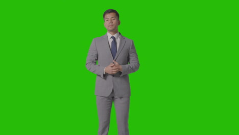 three quarter length portrait of businessman in suit straightening cuffs against green screen