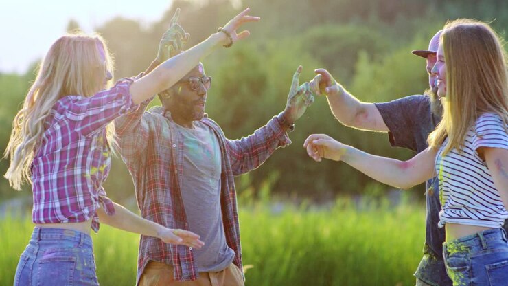 Giovani ragazzi e ragazze multietnici e gioiosi che celebrano il festival di Holi all'aperto nel campo verde con colori vivaci e balli.