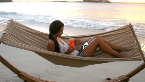 Woman-using-digital-tablet-and-having-mocktail-on-a-hammock