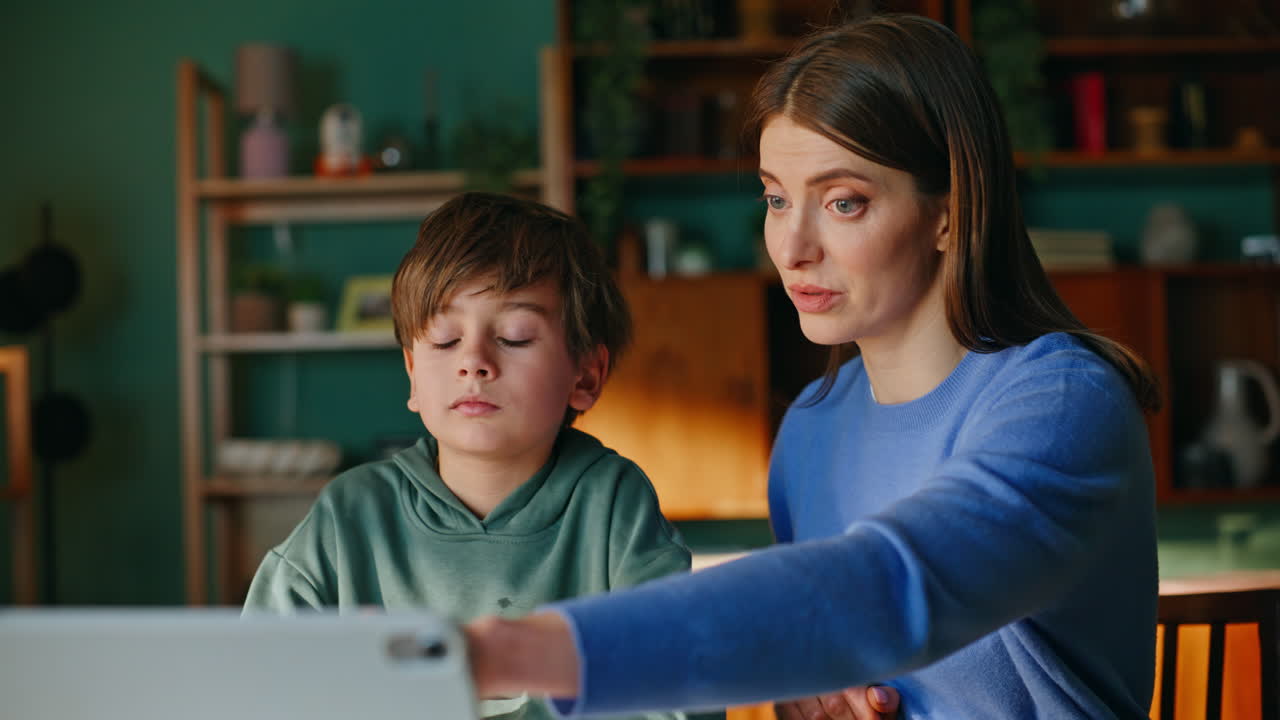 Primo piano di madre e scolaro che studiano online, guardando materiale didattico su un tablet.