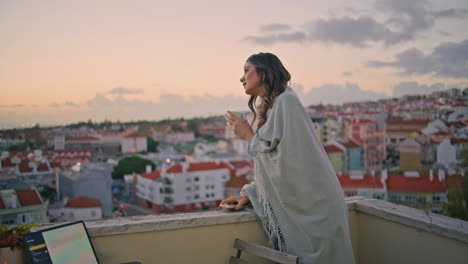 serene woman peeping cityscape balcony with coffee cup in hands. lady waiting