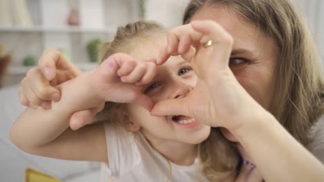 madre e hija están haciendo corazones y mirando a la cámara.