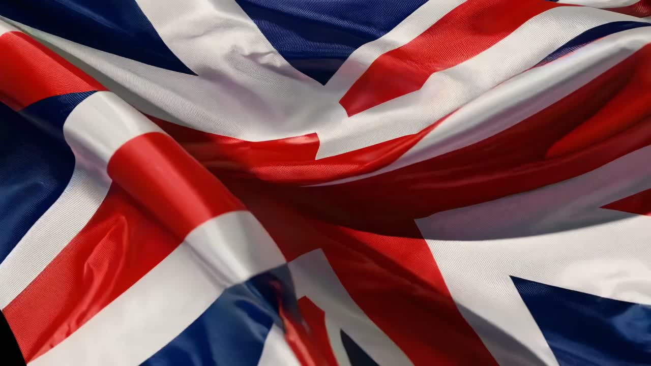 Close-up dinâmico de uma bandeira britânica tremulando, exibindo cores vibrantes e movimento.