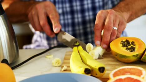 Mid-section-of-man-slicing-a-banana-on-kitchen-worktop