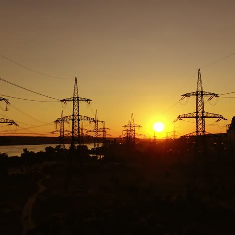 high voltage station at sunset. tall pylons for electricity transmission. silhouette of electric towers over sunset time. camera moving top down.