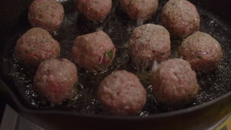 adding spice on top of fried meatballs inside hot frying pan with boiling cooking oil