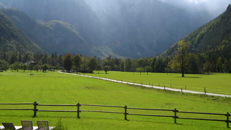 Vista-Panorámica-En-El-Valle-De-Logarska,-Eslovenia,-Prados-Verdes-Con-Bosques-Y-Altas-Montañas-En-El-Fondo,-Piscina-Natural-Con-Tumbonas-En-Frente