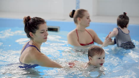 happy middle-aged mother swimming with cute adorable baby in swimming pool. smiling mom and little child, newborn girl having fun together. active family spending leisure and time in spa hotel.