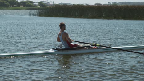 side view of male rower practicing rowing on the lake