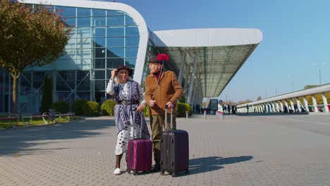 senior pensioner tourists grandmother grandfather using mobile phone make selfie vlog near airport