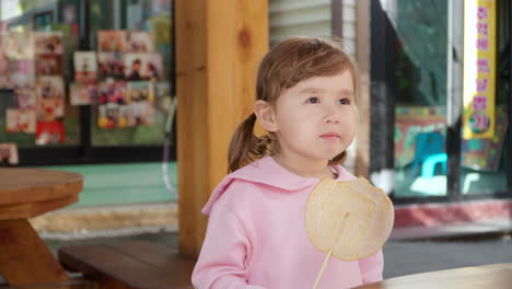 happy smiling child girl eats crunchy circular dalgona sugar candyon stick at gyeongamdong railroad town old market - portrait slow motion