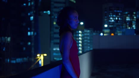 The-Caribbean-city-lights-of-Port-of-Spain,-Trinidad-illuminate-the-background-as-a-Hispanic-girl-stands-on-a-rooftop