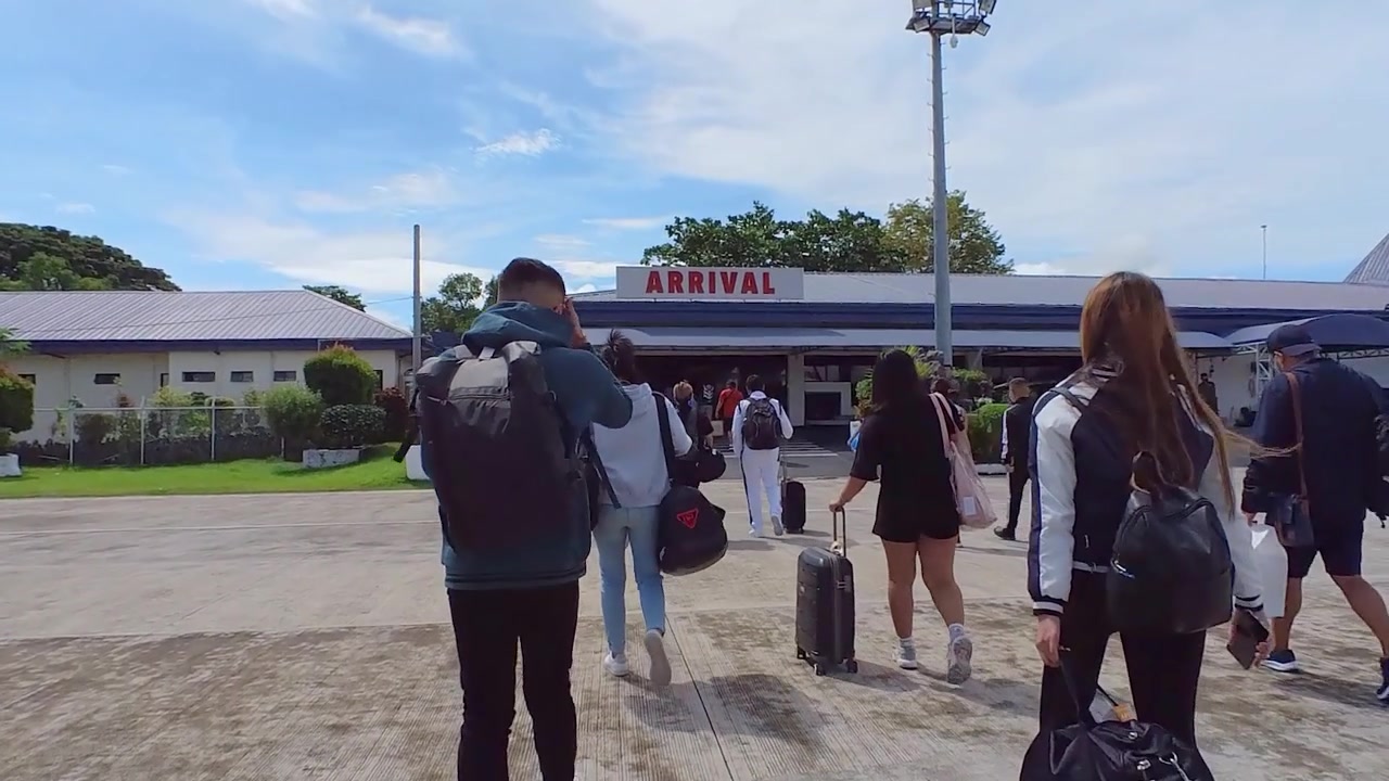 A group of passengers walking towards a building with a arrival signage.