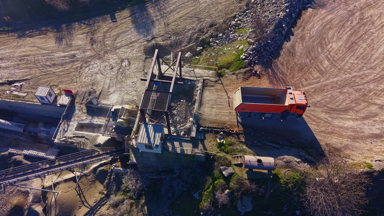 Construction site bustling with activity as a large orange truck unloads materials during bright daylight in a serene landscape
