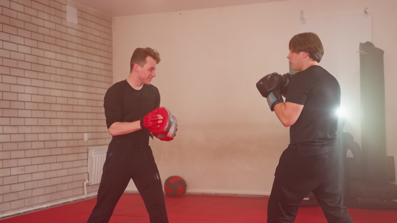 MMA fighters spar during training session, one athlete delivering powerful punch while opponent defends with red pads, demonstrating speed, strength, combat skills, discipline inside martial arts