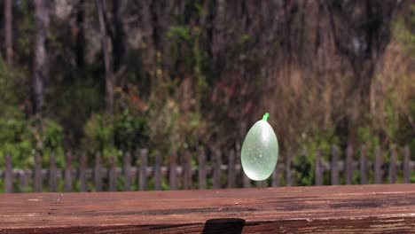 Un-Globo-De-Agua-Verde-Cae-Sobre-Un-Banco-De-Madera-Y-Rebota