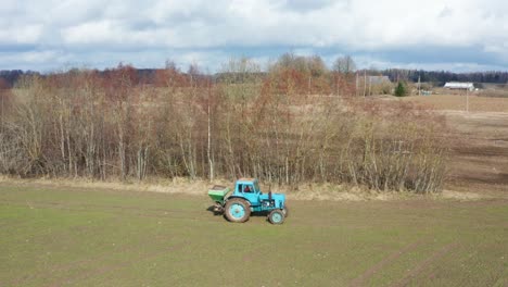 farmer use old tractor equipment to spread granular fertilizer on wheat field