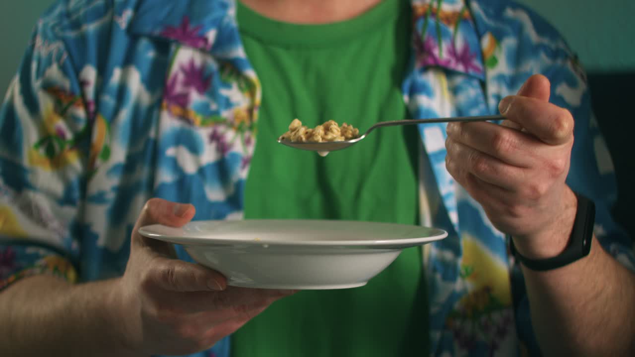 Close up of a Young man holding a bowl full of delicious cereals drops milk with a spoon into a bowl at night detail shot