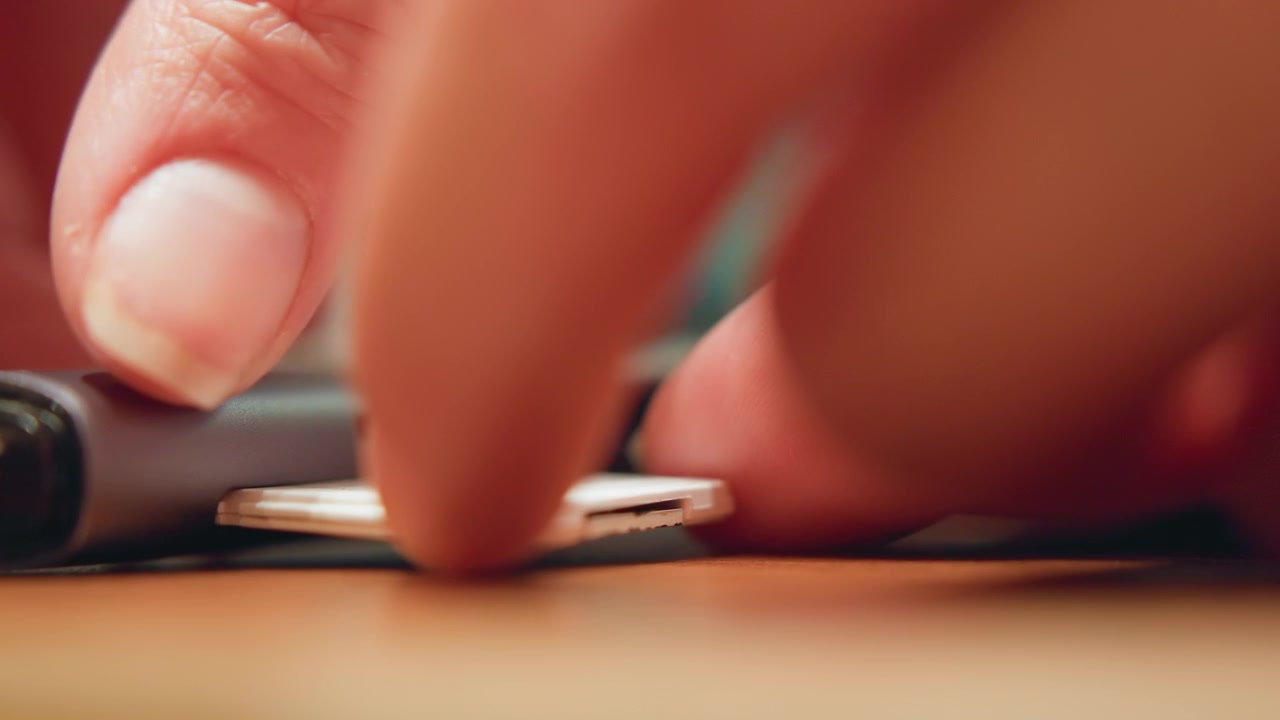 Technician inserting SIM into laptop. Detailed image of hand inserting SIM card into device port. Focused shot capturing technician placing sim card into port of computer on wooden desk