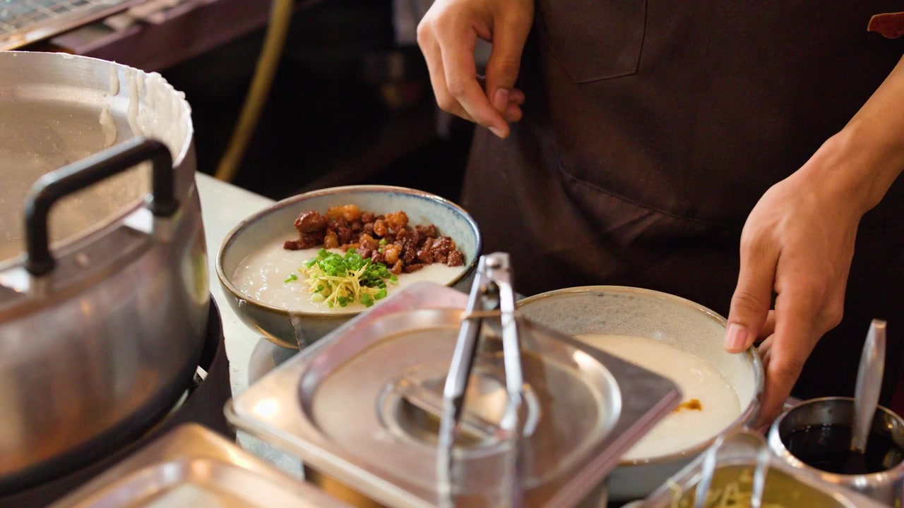 Professional chef adds fresh scallions and ginger to a bowl of pork congee in kitchen.
