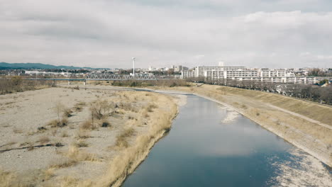 Drone-Volando-Sobre-El-Río-Tama-Con-La-Línea-Ferroviaria-Itsukaichi-En-La-Distancia-En-Tokio,-Japón