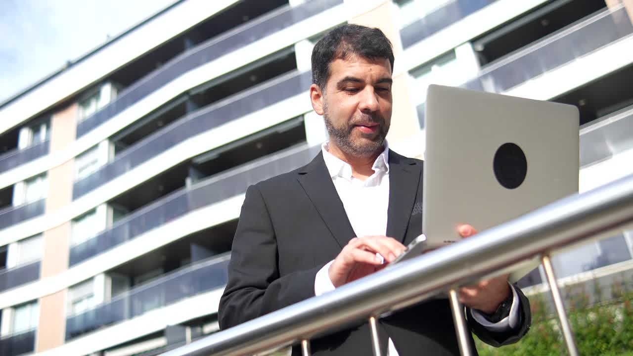 Businessman working on a laptop outdoors in front of a modern building