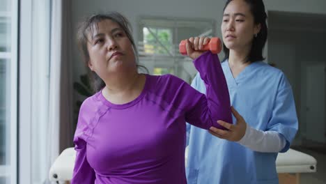 fisioterapeuta asiática ayudando a una paciente a ejercitar los brazos con pesas en la cirugía